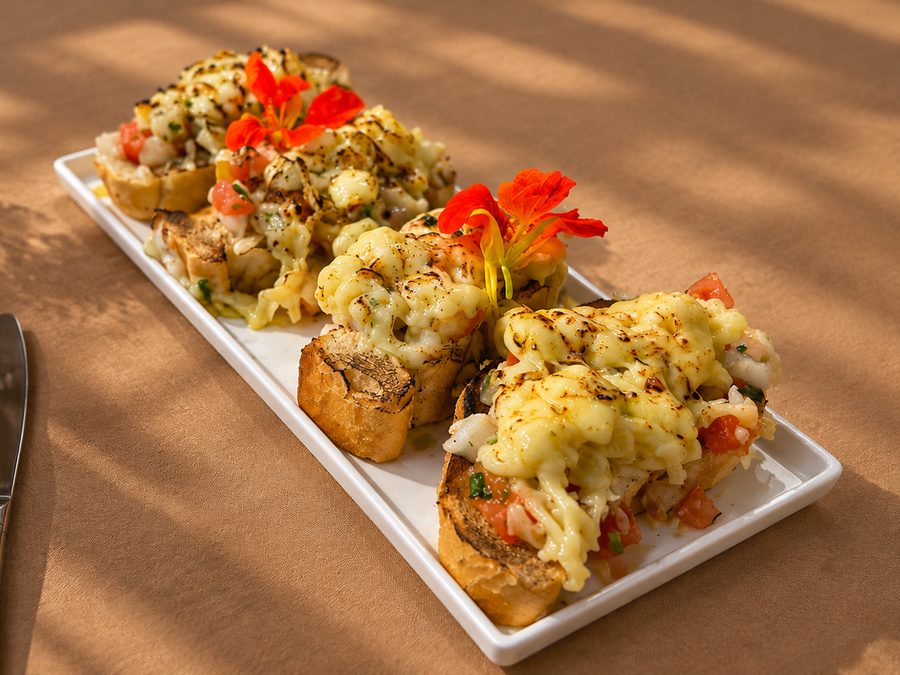 Bruschettas gratinadas servidas em travessa branca com flor comestível