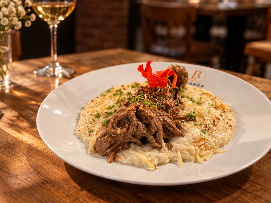 Costela bovina ao molho rôti servida sobre creme de arroz em prato branco